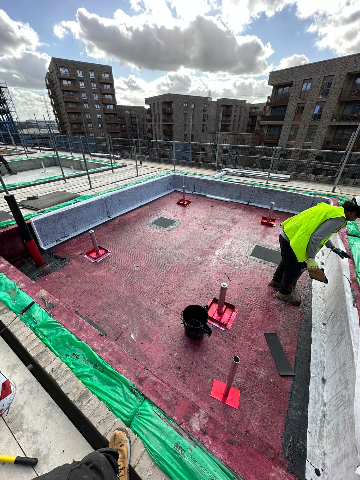 Waterproofing work progressing around the upstands of a flat roof.